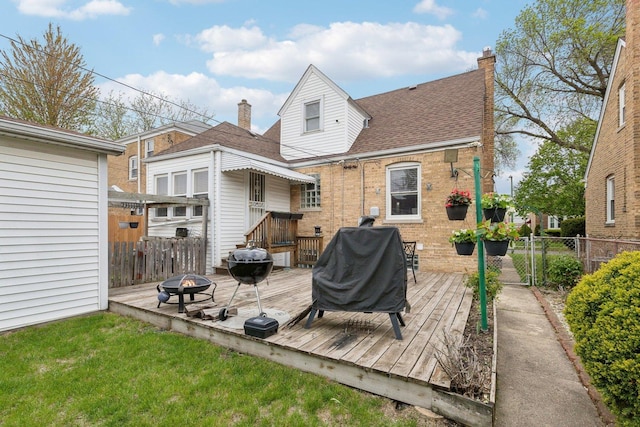 rear view of property featuring roof with shingles, fence, brick siding, a wooden deck, and an outdoor fire pit