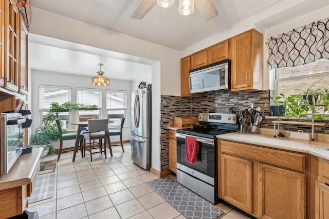 kitchen featuring stainless steel appliances, light tile patterned flooring, light countertops, and ceiling fan with notable chandelier