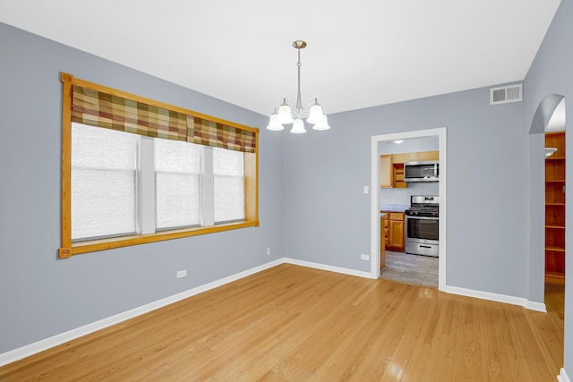 unfurnished dining area featuring arched walkways, a chandelier, light wood finished floors, and baseboards