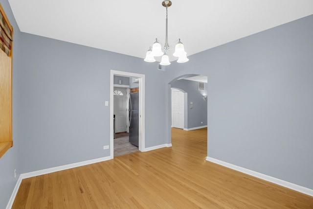 unfurnished dining area with arched walkways, a chandelier, baseboards, and light wood-type flooring