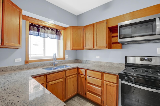 kitchen featuring stainless steel appliances, a sink, light stone counters, and light wood-style flooring