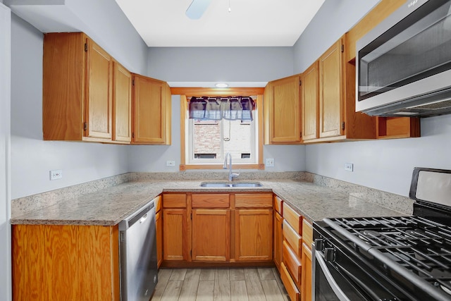 kitchen with appliances with stainless steel finishes, a sink, light countertops, light wood finished floors, and a ceiling fan
