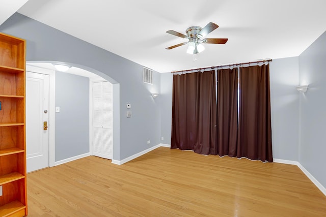 spare room with arched walkways, a ceiling fan, light wood finished floors, and baseboards