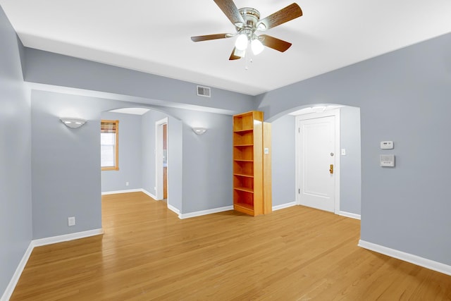 empty room featuring arched walkways, light wood-style flooring, a ceiling fan, and baseboards
