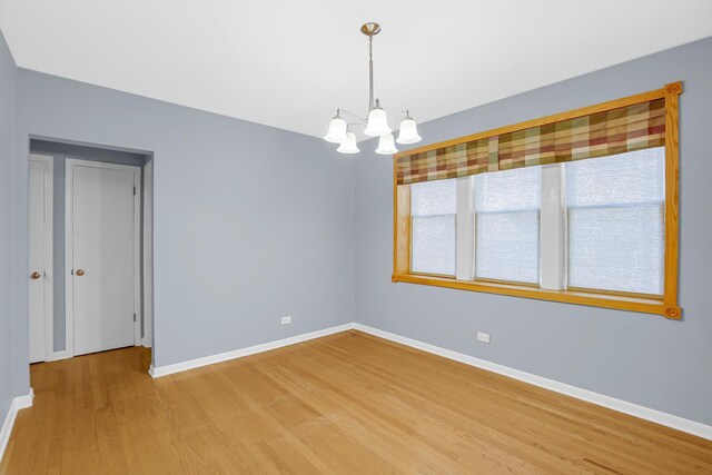 spare room featuring a chandelier, baseboards, and light wood-type flooring