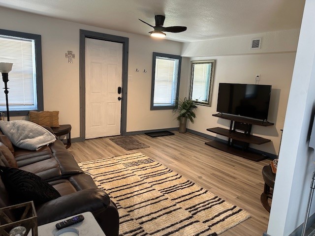 living room featuring light wood finished floors, a wealth of natural light, visible vents, and a ceiling fan