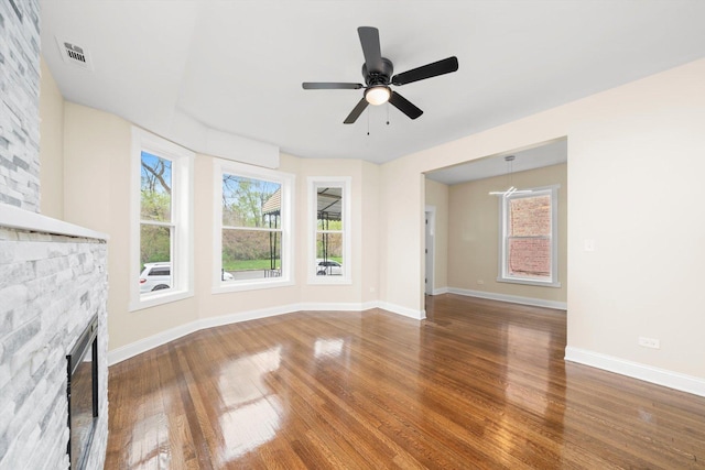 unfurnished living room with visible vents, wood finished floors, a stone fireplace, baseboards, and ceiling fan