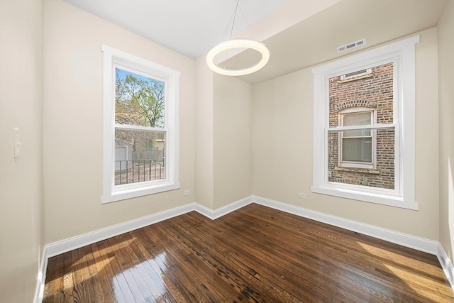 spare room featuring visible vents, baseboards, and dark wood-style floors