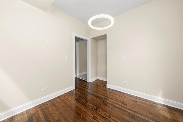empty room featuring baseboards, dark wood-style floors, and an inviting chandelier