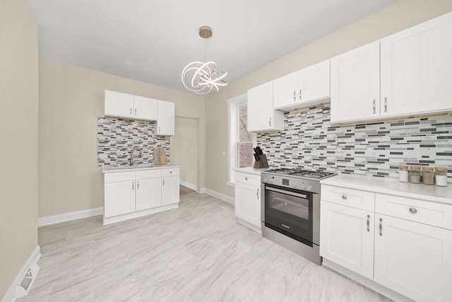 kitchen with an inviting chandelier, gas stove, white cabinetry, light countertops, and tasteful backsplash