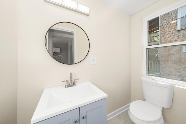 half bath featuring baseboards, toilet, and vanity