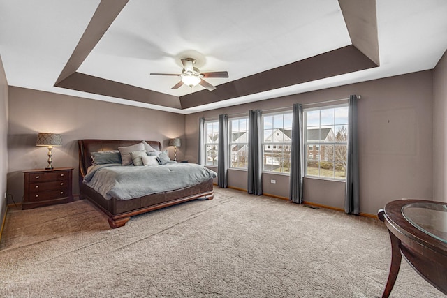 bedroom featuring a tray ceiling, multiple windows, baseboards, and carpet floors