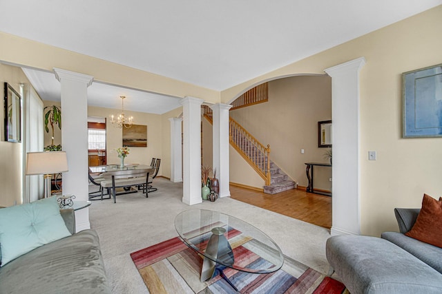 carpeted living room featuring baseboards, stairway, an inviting chandelier, and decorative columns