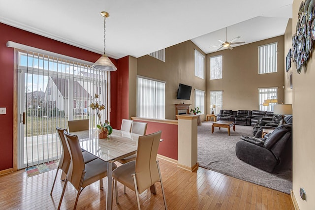 dining space with a fireplace, ceiling fan, baseboards, and light wood-type flooring