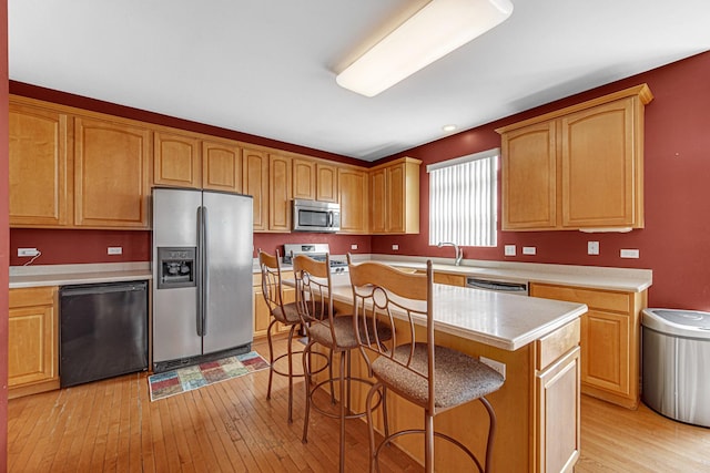 kitchen with a breakfast bar area, a center island, light wood-style flooring, stainless steel appliances, and light countertops