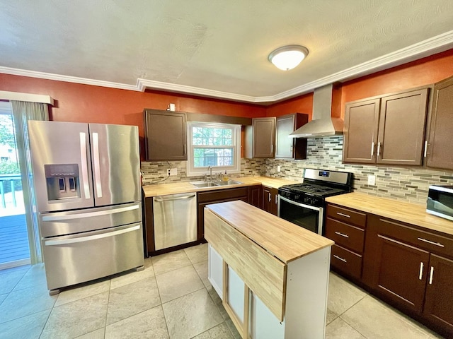 kitchen featuring stainless steel appliances, wall chimney exhaust hood, wooden counters, a sink, and tasteful backsplash