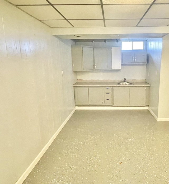 kitchen featuring baseboards, a paneled ceiling, light countertops, and a sink