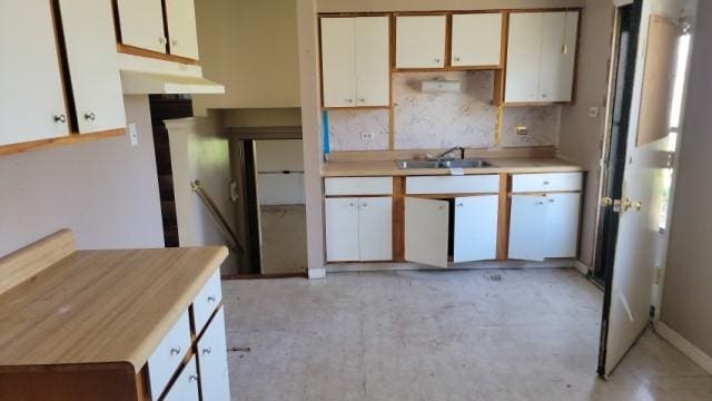 kitchen featuring decorative backsplash, a sink, light countertops, white cabinets, and concrete floors