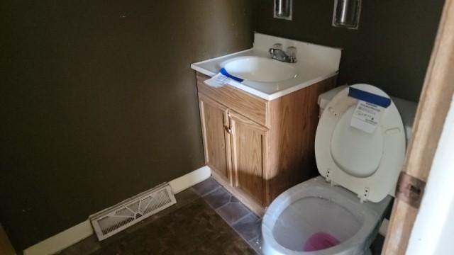 bathroom with visible vents, vanity, toilet, baseboards, and stone finish flooring