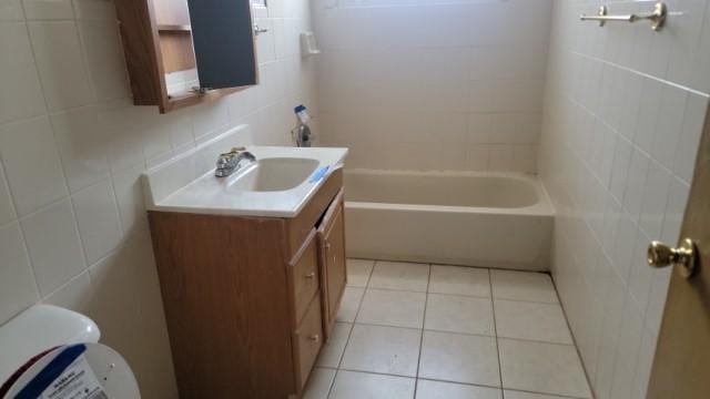 full bathroom with vanity, toilet, tile walls, a tub, and tile patterned floors