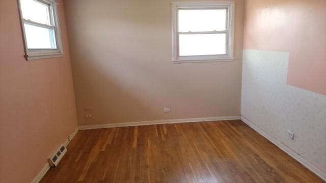 spare room featuring baseboards, visible vents, wood finished floors, and a wealth of natural light