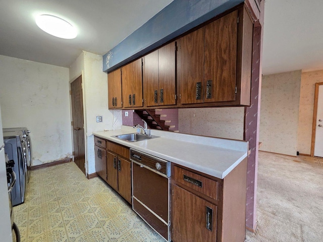 kitchen with washing machine and dryer, dishwasher, a sink, light countertops, and baseboards
