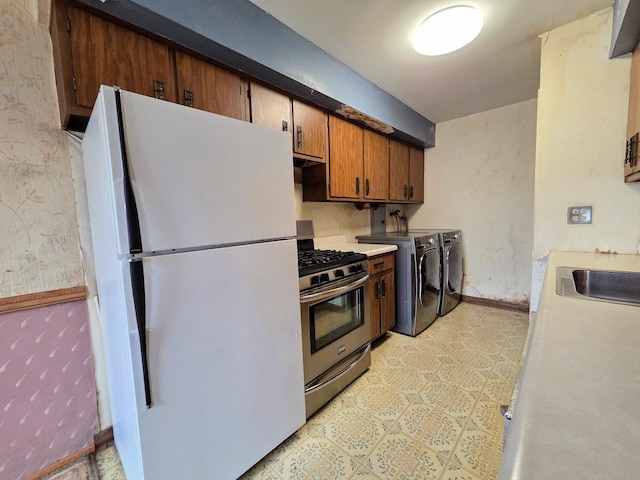 kitchen featuring washing machine and clothes dryer, stainless steel gas range oven, light countertops, a sink, and freestanding refrigerator