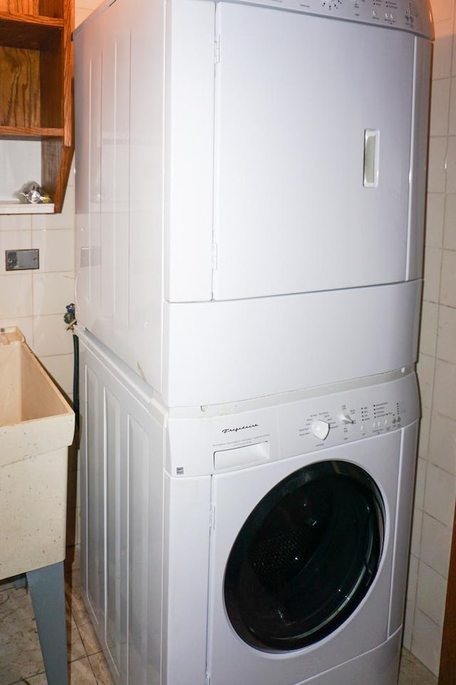 laundry room with stacked washing maching and dryer, tile walls, laundry area, and a sink