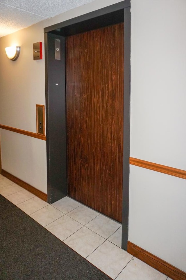 hallway featuring baseboards, light tile patterned floors, and elevator