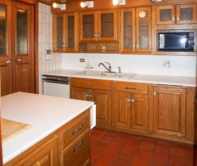 kitchen with black microwave, brown cabinets, dishwasher, light countertops, and a sink