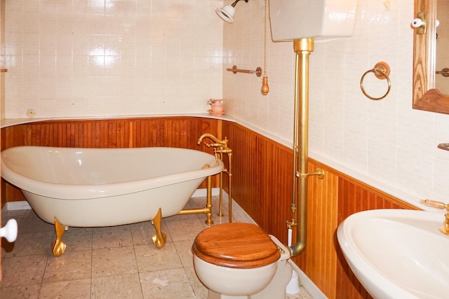 full bath featuring a sink, a freestanding tub, wainscoting, and wood walls