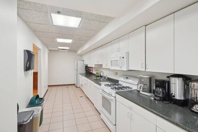 kitchen with white appliances, a drop ceiling, a sink, dark countertops, and white cabinets