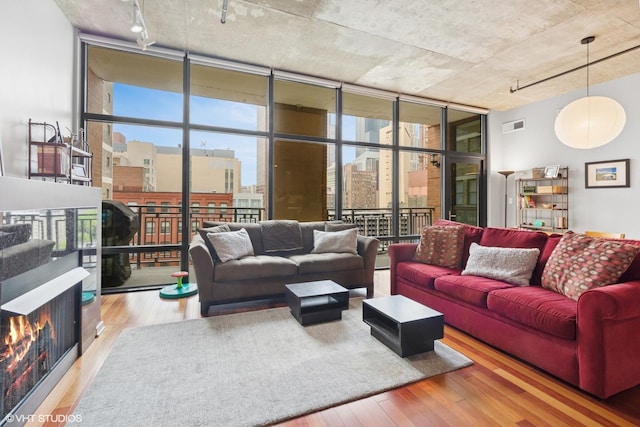 living room with track lighting, wood finished floors, floor to ceiling windows, a lit fireplace, and healthy amount of natural light