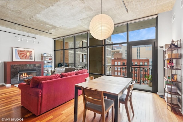 dining space with rail lighting, expansive windows, wood-type flooring, a fireplace, and baseboards