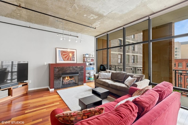 living area featuring track lighting, wood finished floors, a tiled fireplace, baseboards, and expansive windows