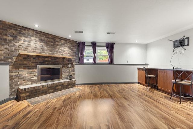 unfurnished living room featuring a fireplace, indoor bar, wood finished floors, and visible vents