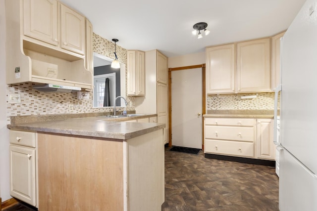 kitchen with backsplash, cream cabinets, a sink, freestanding refrigerator, and a peninsula