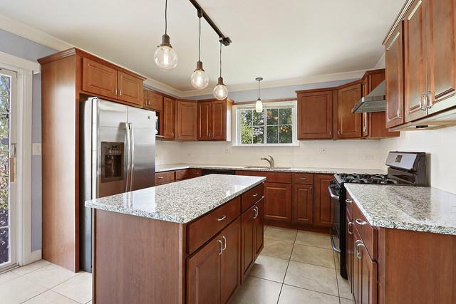 15535 Homan Ave, Markham, IL 60428 - kitchen featuring appliances with stainless steel finishes, light tile patterned floors, light stone countertops, a kitchen island, and ornamental molding
