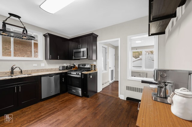 kitchen with stainless steel appliances, a sink, radiator, dark cabinetry, and dark wood-type flooring