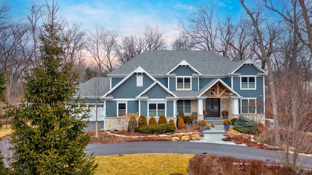 craftsman-style home featuring a lawn, a shingled roof, covered porch, and stone siding