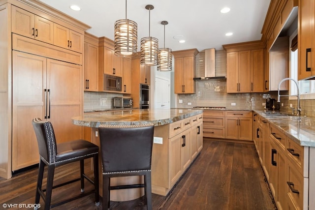 kitchen with a center island, light stone countertops, a sink, built in appliances, and wall chimney exhaust hood