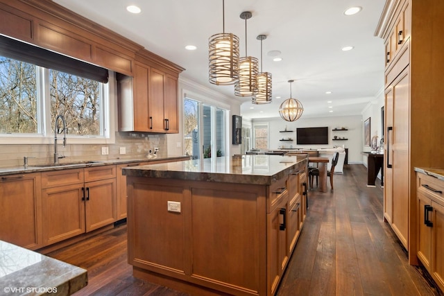 kitchen featuring an inviting chandelier, open floor plan, a center island, dark stone counters, and a sink