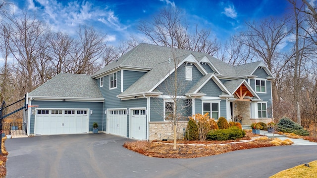 craftsman house with a shingled roof, an attached garage, driveway, and stone siding
