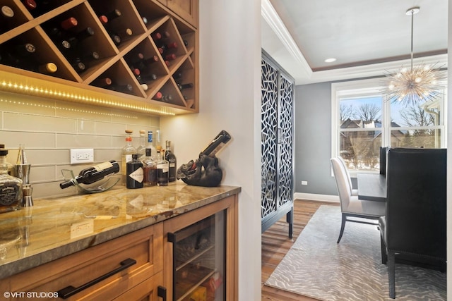 interior space with a dry bar, beverage cooler, ornamental molding, baseboards, and dark wood-style floors