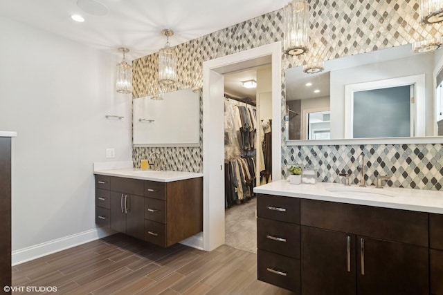 full bathroom with decorative backsplash, wood finished floors, two vanities, a sink, and baseboards