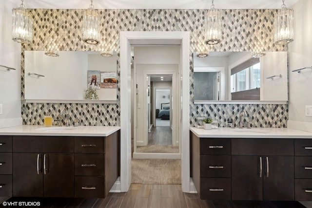 ensuite bathroom with a sink, tasteful backsplash, and two vanities
