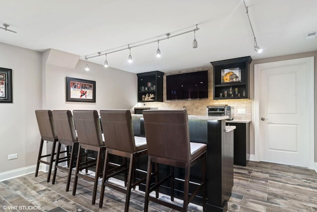 bar with indoor wet bar, backsplash, wood finished floors, and track lighting
