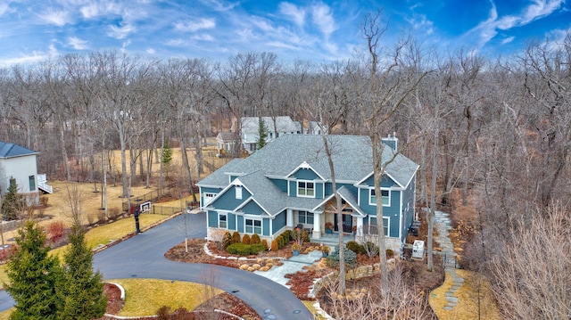 view of front of home with curved driveway, a shingled roof, covered porch, and a chimney