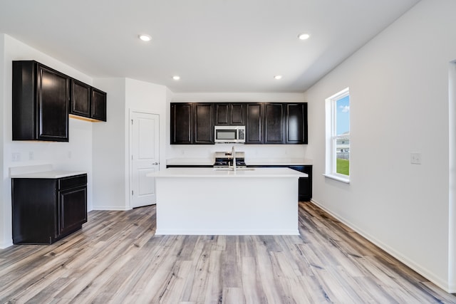 kitchen featuring a sink, light countertops, baseboards, stainless steel microwave, and light wood-style flooring