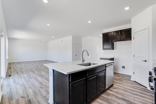 kitchen featuring stainless steel dishwasher, a sink, light countertops, light wood-style floors, and an island with sink